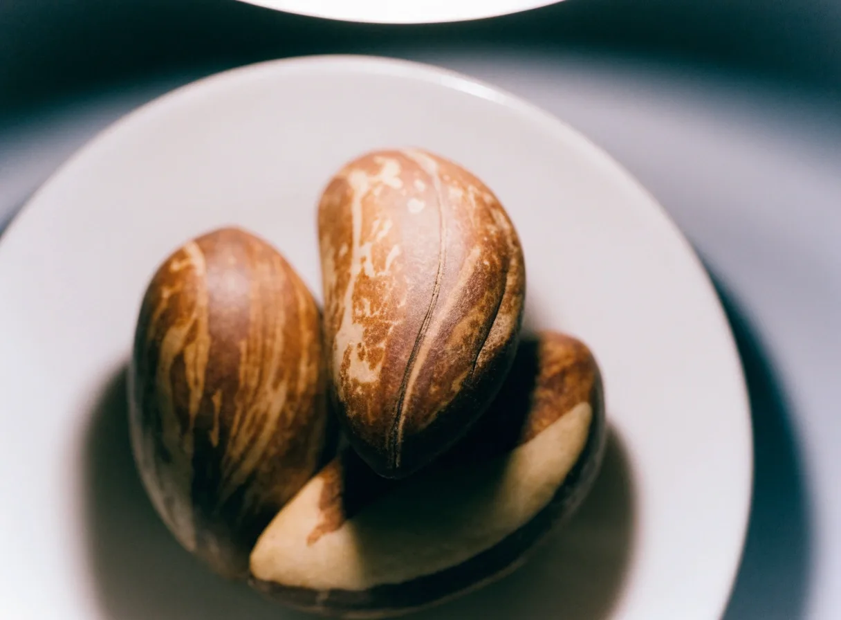 Three Brazil nuts on a matte white plate under one overhead lamp